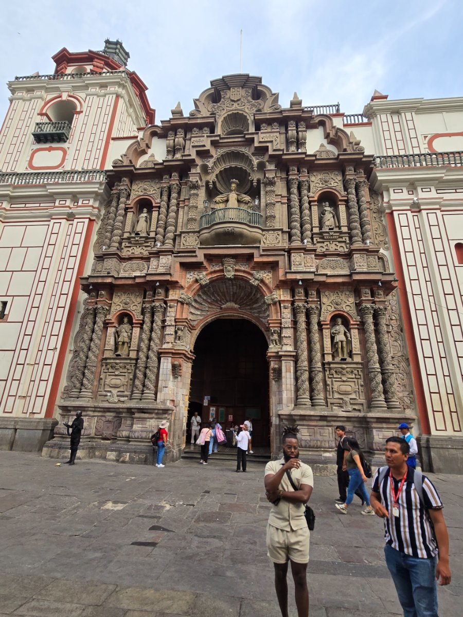 A person standing in front of a grand, ornate church facade with intricate carvings and statues, likely in Lima's historic center.
